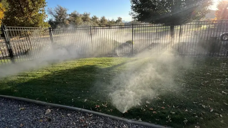 Irrigation system watering a lawn with fence and trees in Western Colorado.