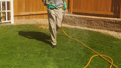 Lawn care provider applying treatment near a fence on Western Colorado bermuda turf.