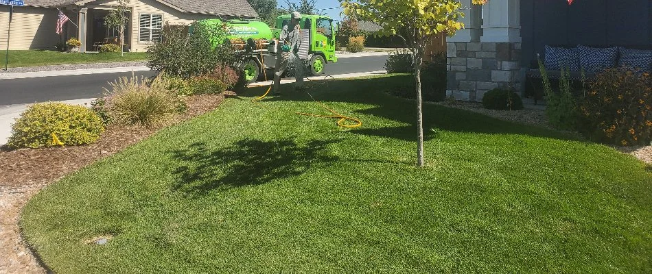 A lawn care provider in Grand Junction, CO, in front of a green truck, applying treatment to a lawn.